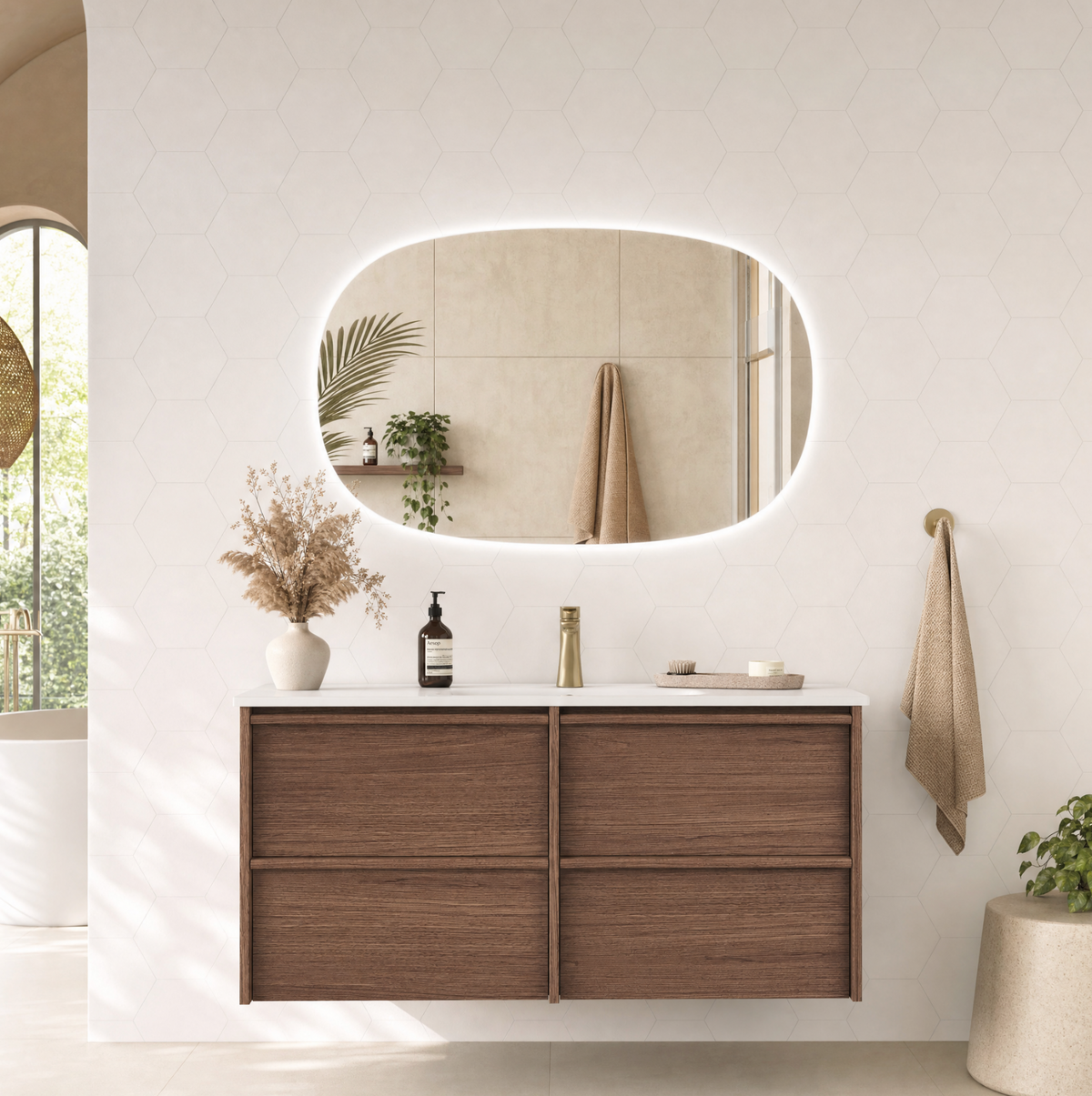 A modern floating bathroom vanity with a white countertop and wood-grain doors, set against a white hexagonal-tiled wall with an illuminated oval mirror. A beige towel hangs on a gold ring holder, and a small potted plant sits on a concrete side table.