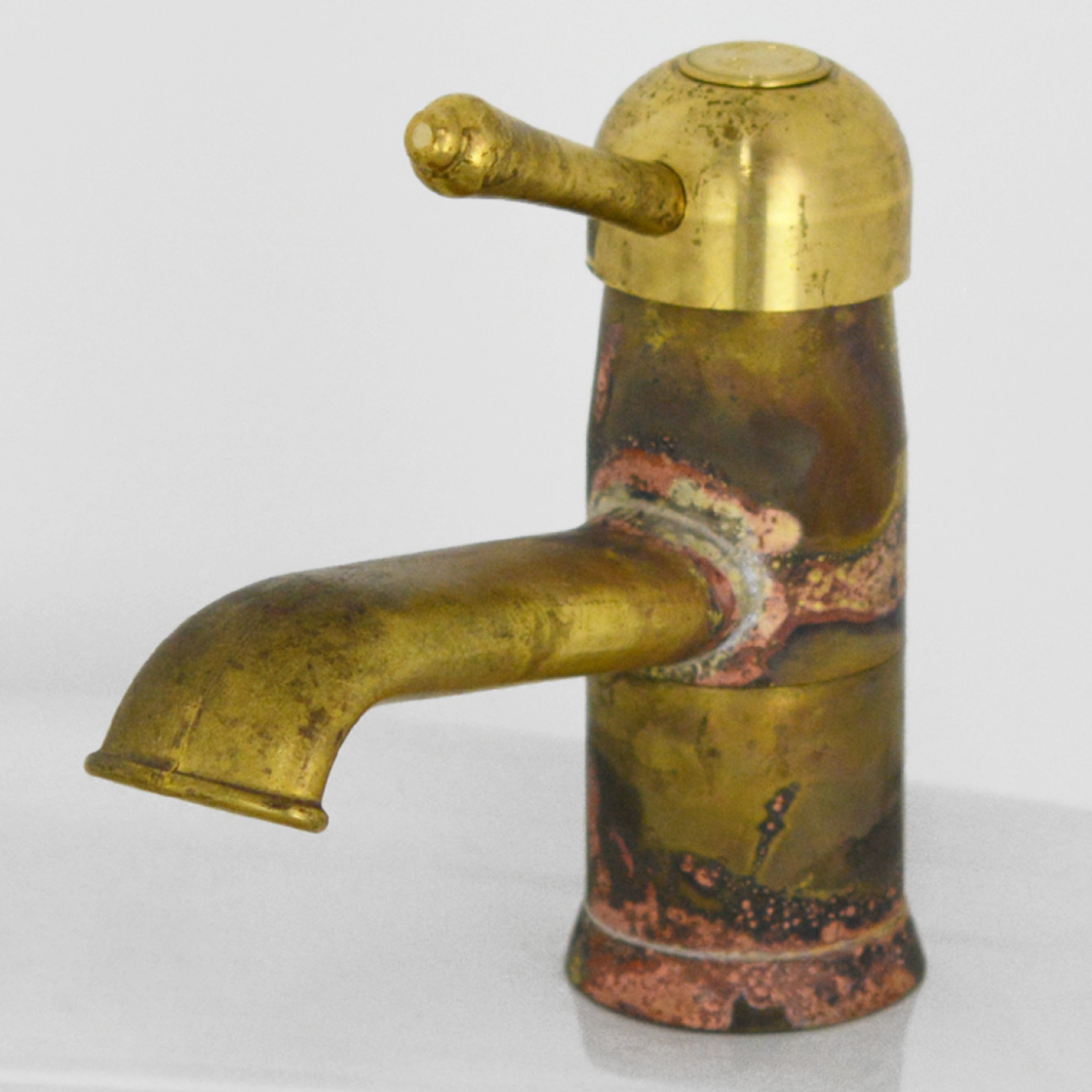 A vintage-style brass basin mixer tap with a curved spout and a single lever handle, featuring a distressed patina with copper and greenish oxidation.