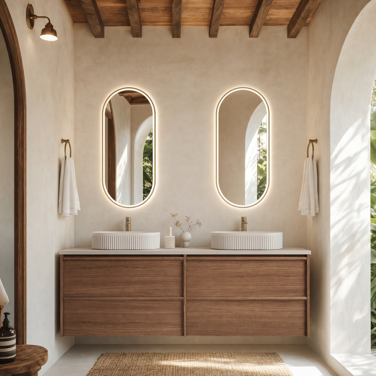 A modern bathroom vanity with two oval backlit mirrors, a double white vessel basins, a floating wood cabinet, and a woven rug, set in a warm, sunlit room with exposed wood ceiling beams.